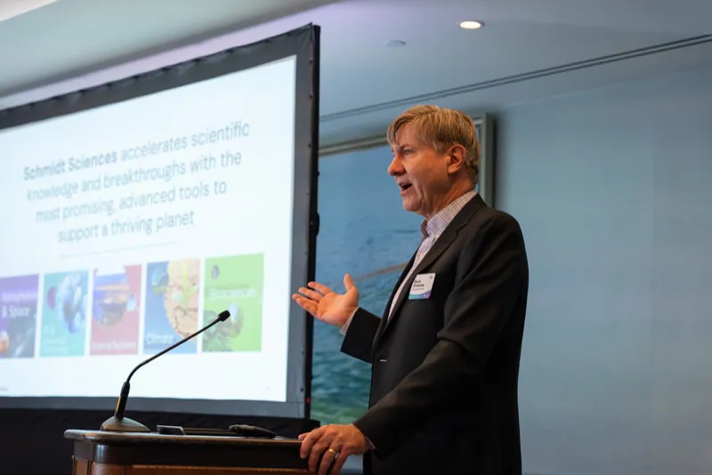 A speaker at the podium presenting a slide about Schmidt Sciences