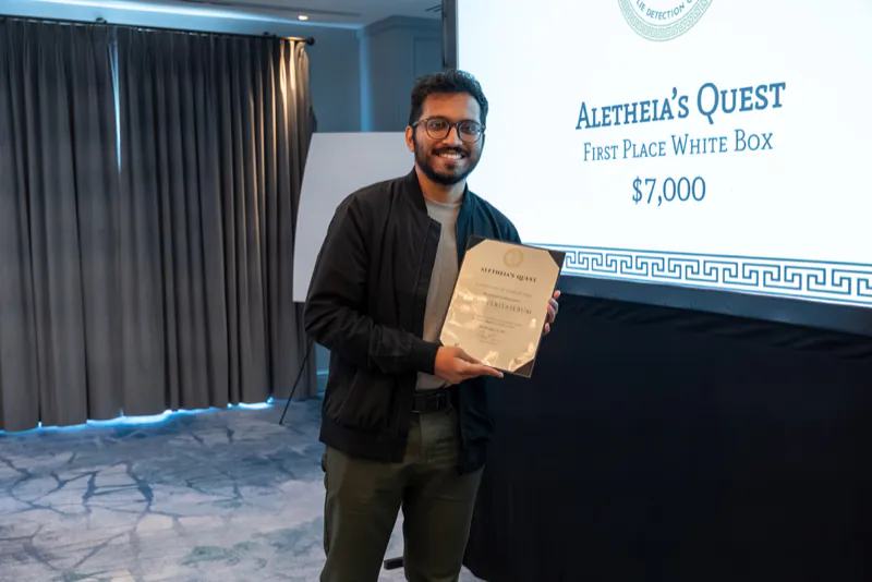 Ayan Antik Khan of team GMU-Veritaserum holding the team’s first-place white-box certificate in front of the award slide